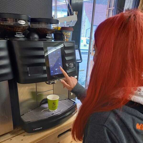 Frau mit roten Haaren lässt einen Kaffee mit einem coffee to go Becher heraus.